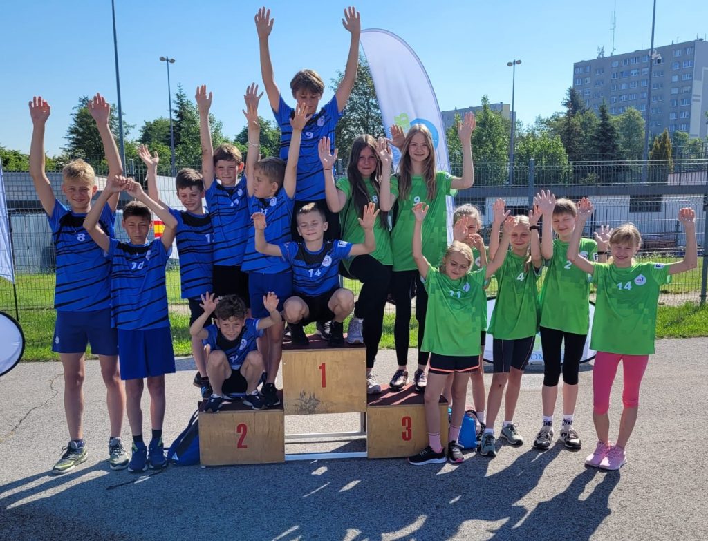 Młodzi sportowcy w zielonych i niebieskich strojach świętują na podium.