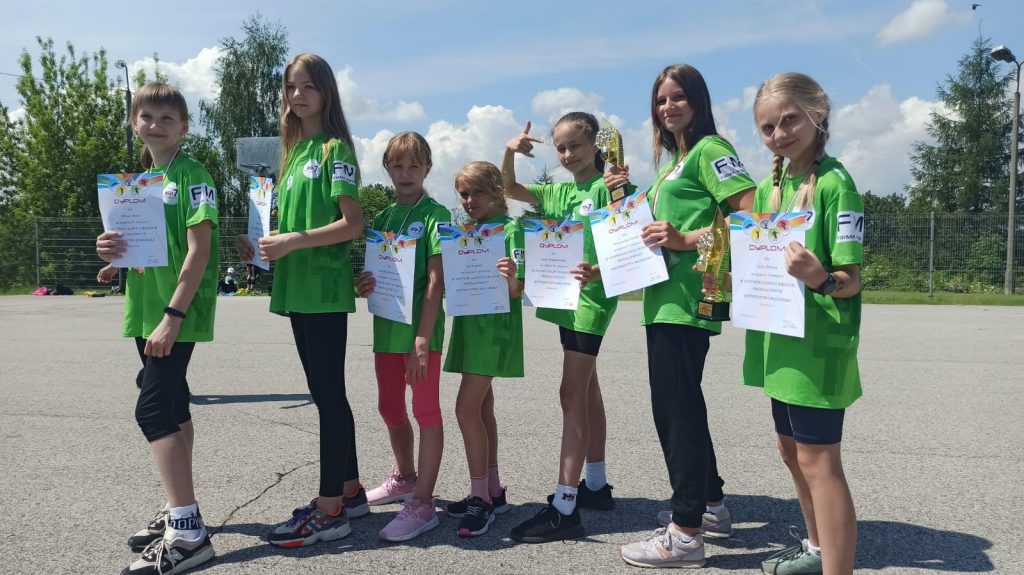 Młodzi sportowcy w zielonych strojach z dyplomami po zawodach.