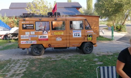 Pomarańczowy samochód uczestników rajdu Złombol, ozdobiony oznaczeniami sponsorów.