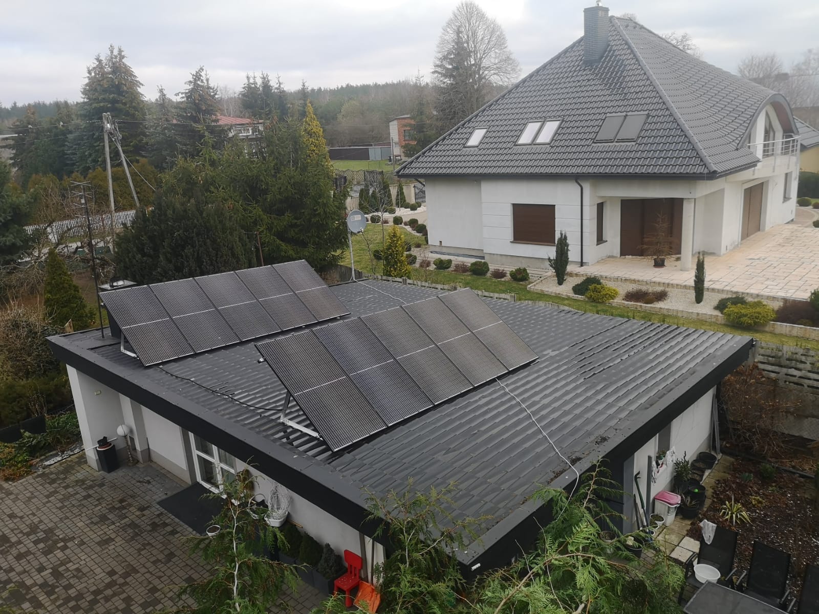 Instalacja fotowoltaiczna na dachu niskiego budynku obok domu.